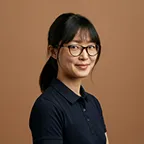 30d75afe-da32-46fe-851c-76d6b9d6aa6d.Portrait of a woman with glasses wearing a navy shirt against warm bac